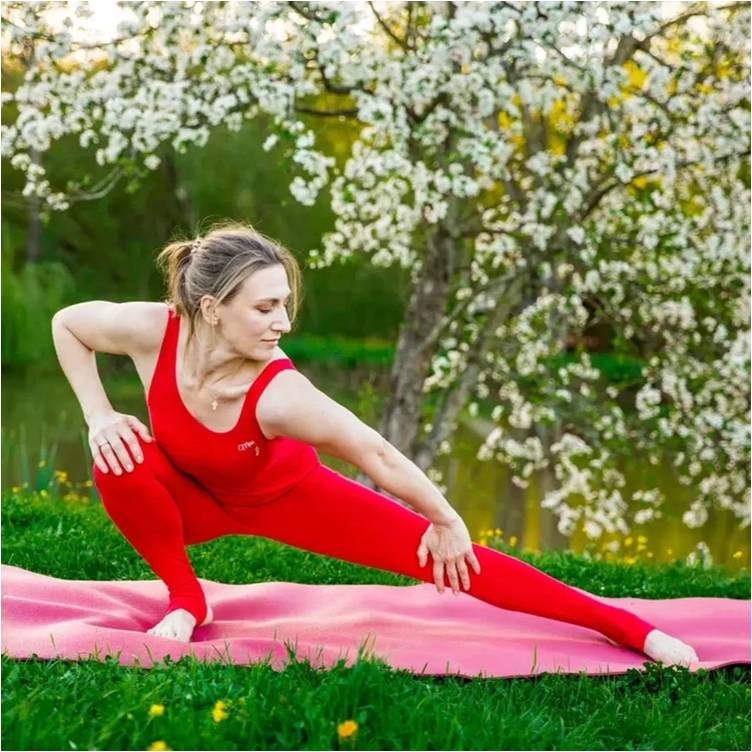 Девушка в красном спортивном костюме выполняет позу йоги.