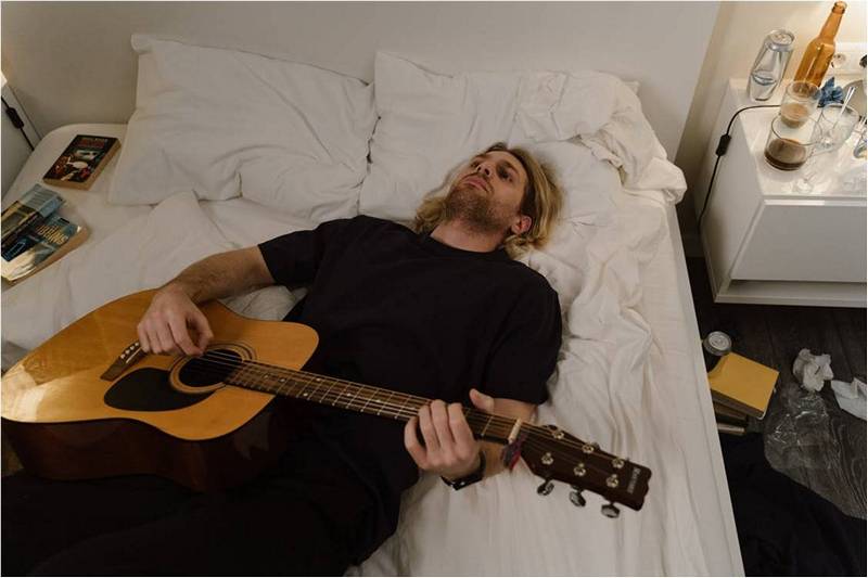 Мужчина с гитарой лежит на кровати.