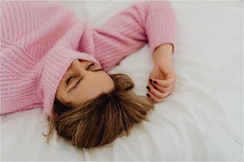 Девушка в розовом свитере спит в кровати.