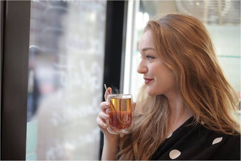 Девушка пьет чай и улыбается, это польза чая для здоровья.