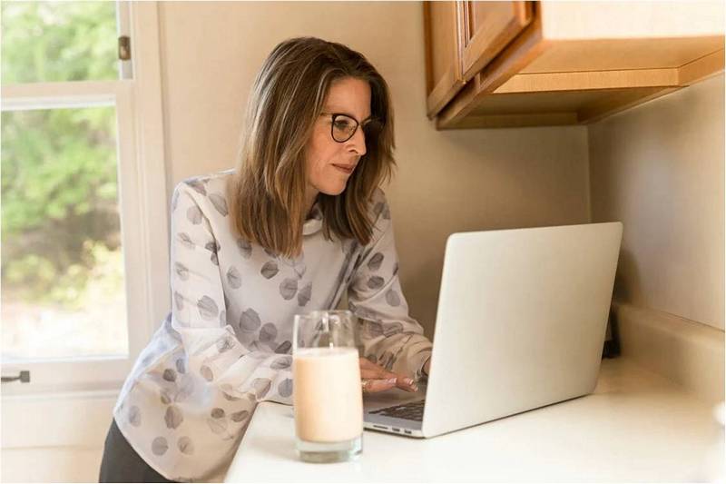 Женщина с ноутбуком на кухне, перед ней стакан молока.