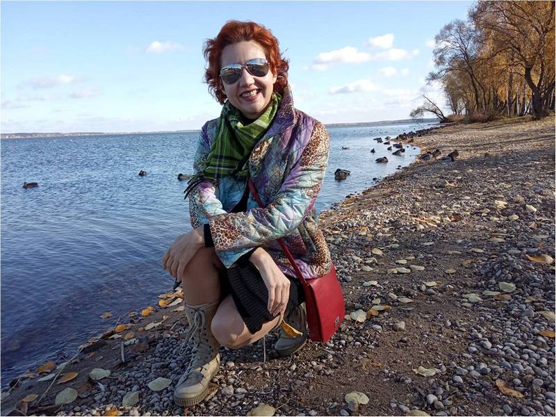 Девушка с красной сумкой сидит на берегу.