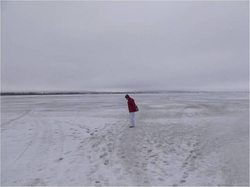 Девушка в красной куртке смотрит на замершее море.